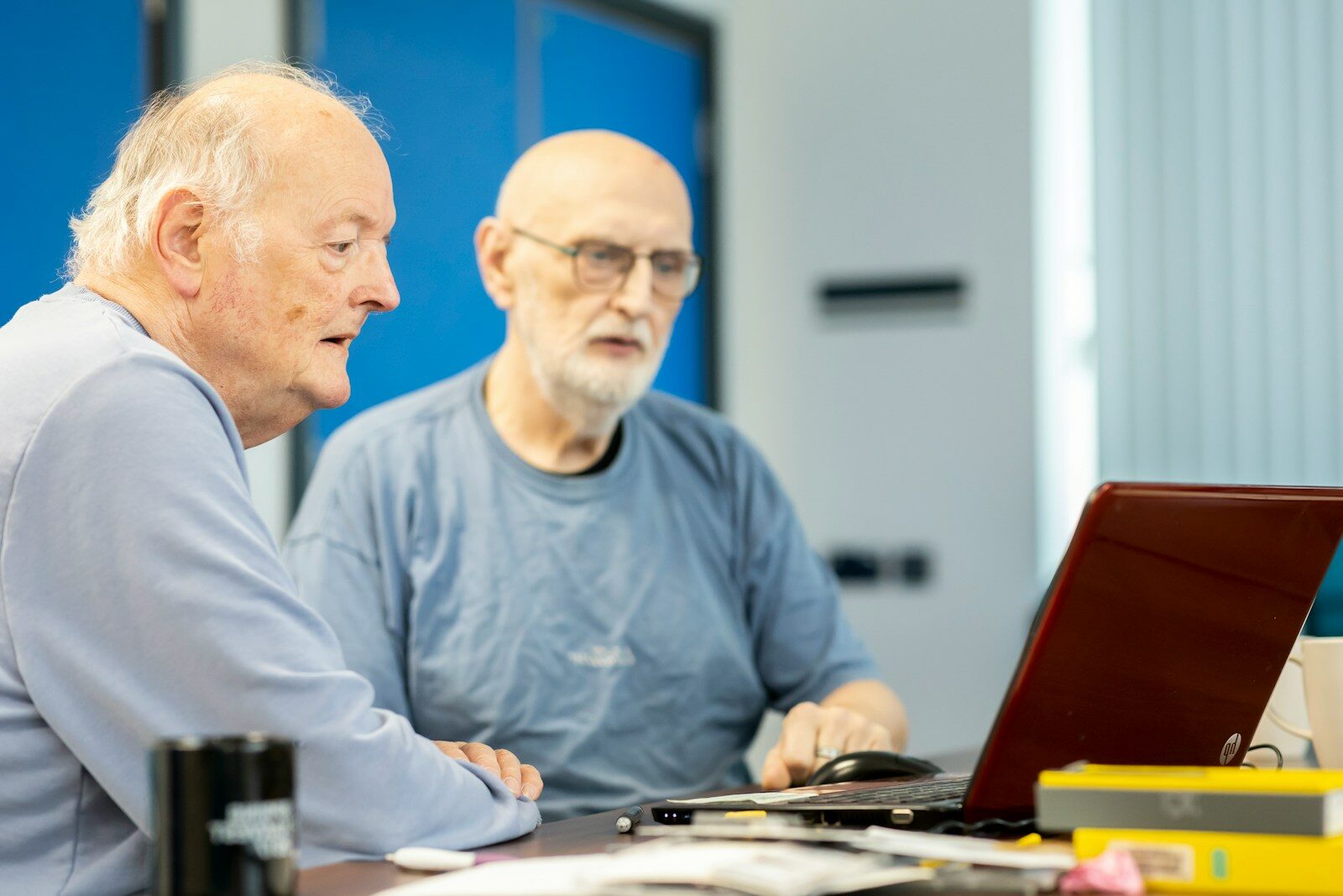 two men sitting at a table looking at a laptop