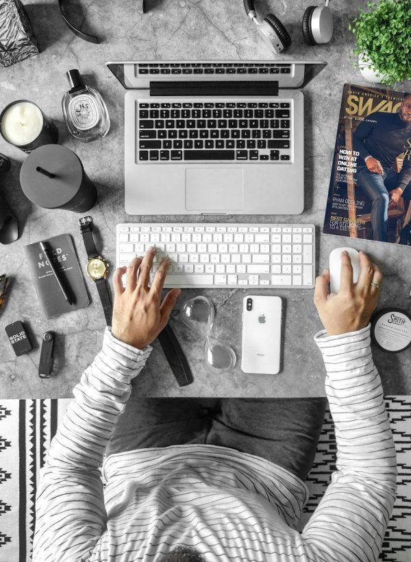 Overhead view of an organized desk with tech gadgets, fashion magazine, and accessories for modern working lifestyle.